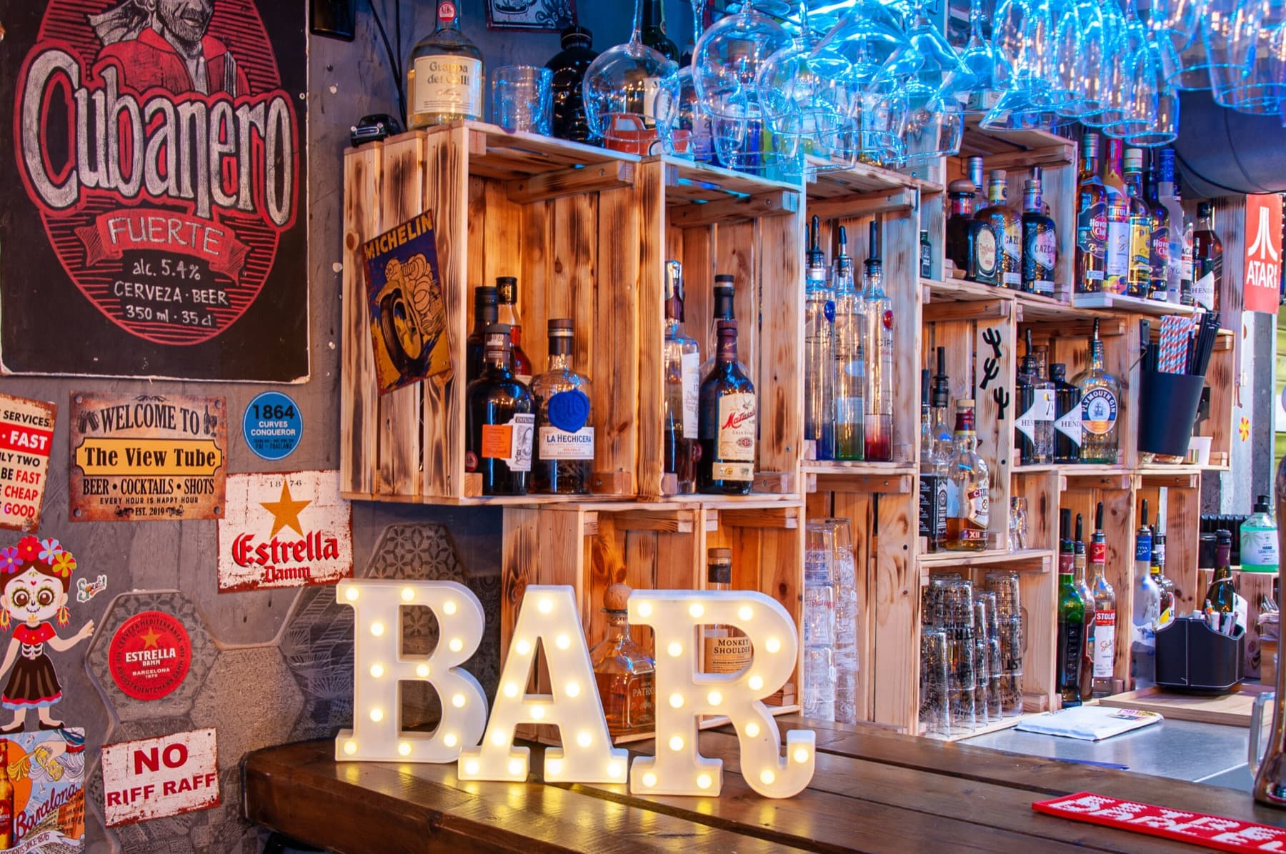 The View Tube bar: illuminated BAR marquee letters, crates of bottles, a Cubanero beer sign and blue neon.