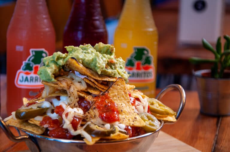 A loaded plate of nachos with guacamole, sour cream and jalapenos.