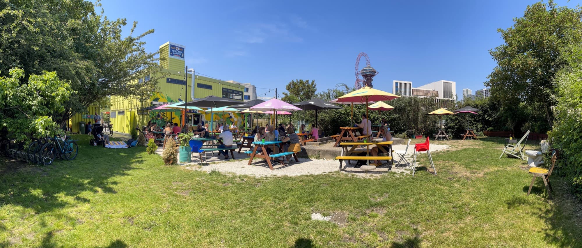 The View Tube beer garden: picnic benches and parasols on the green, with the Olympic Park Orbit and London skyline behind.