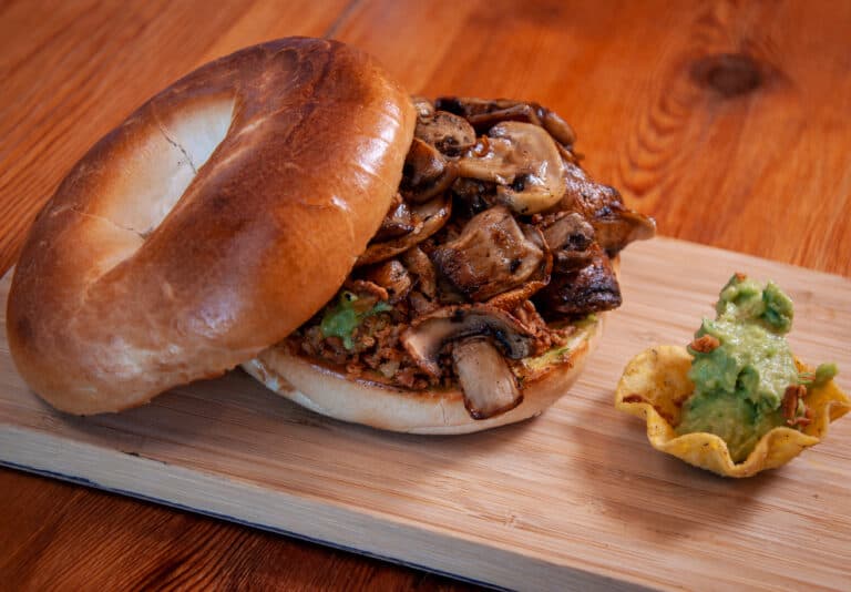 A toasted bagel with mushroom, egg, guacamole and crispy onions.